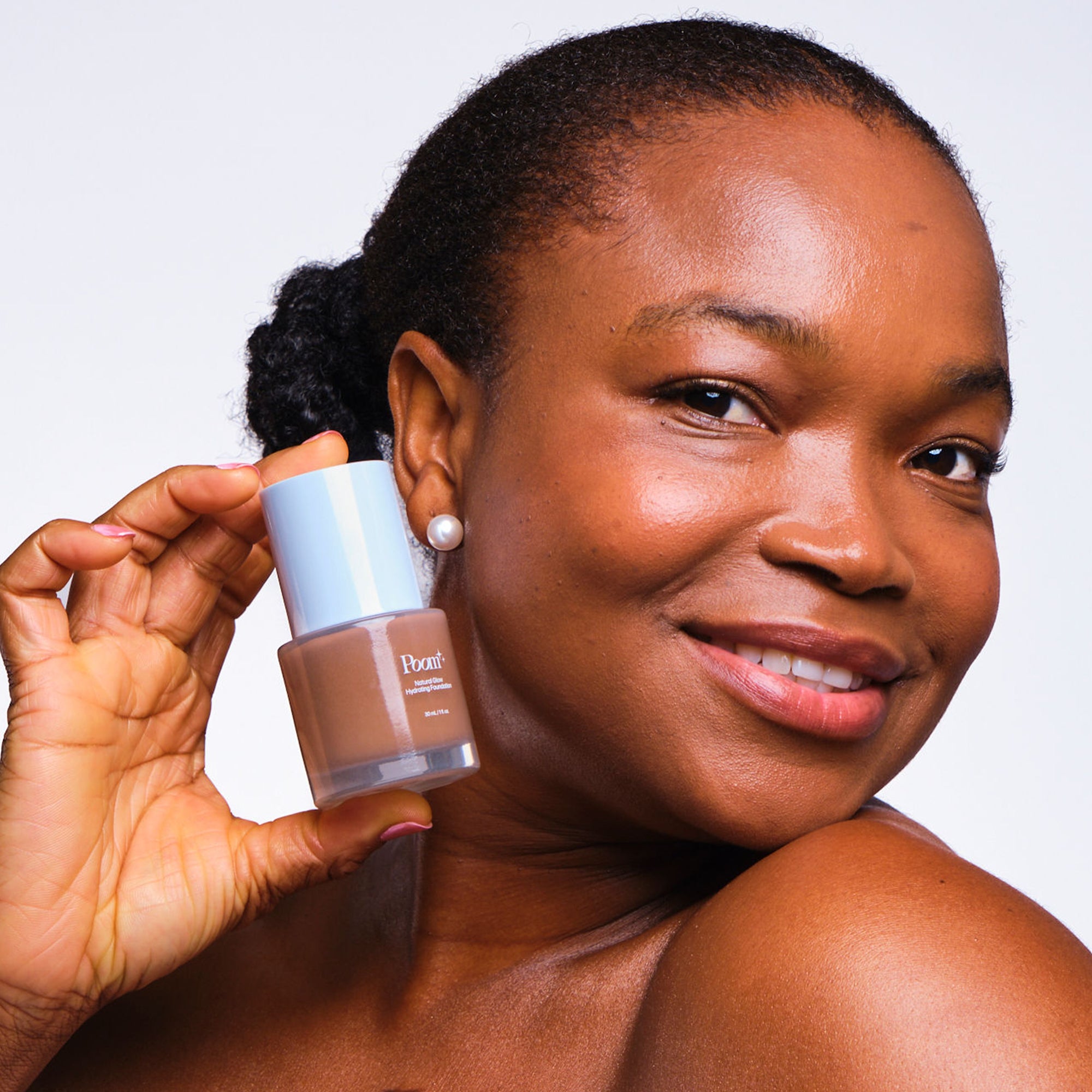 Woman holding a bottle of foundation with a neutral background wearing shade 500