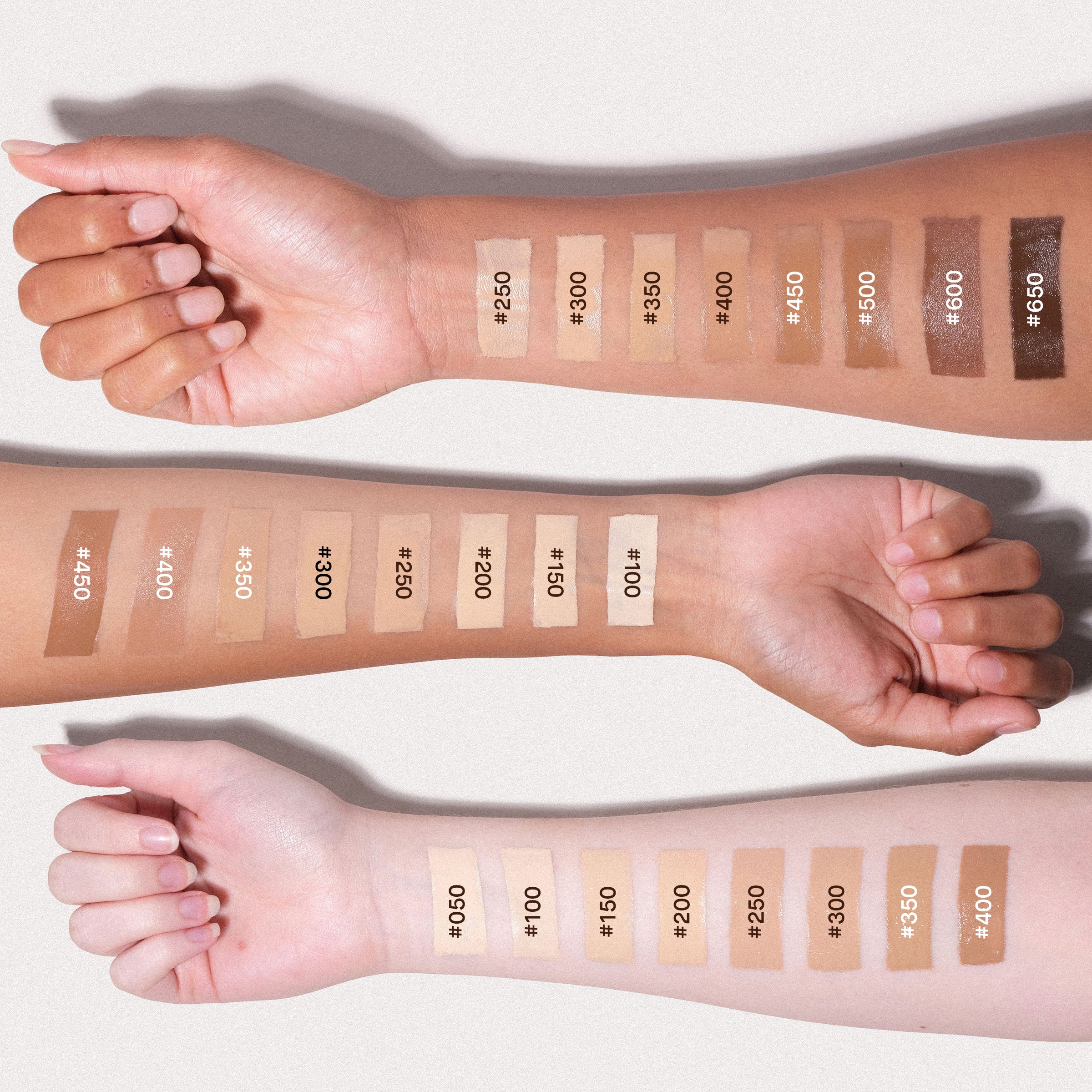 Three human forearms are arranged horizontally against a light neutral background, each showing a row of square makeup swatches labeled with shade numbers ranging from #400 to #650. The swatches display a gradient of skin-tone makeup colors, including light beige, medium tan, and deep brown.